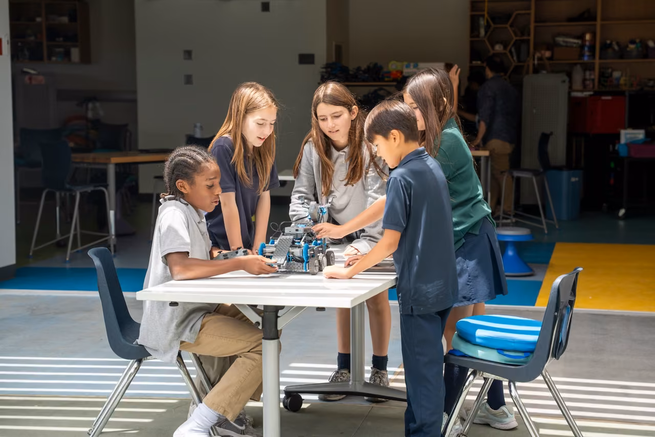 Five students work together on a wheeled robot at a table on the Innovation Lab Patio.