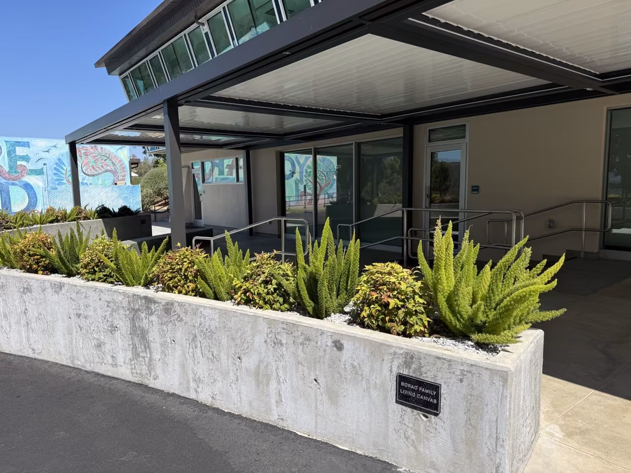 The covered ILab patio, planted concrete wall, and Borao Family Living Canvas sign, with the colorful mural beyond.