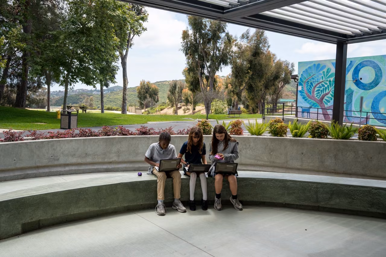 Three students use computers beneath the patio pergola, with the Living Canvas Wall beyond.