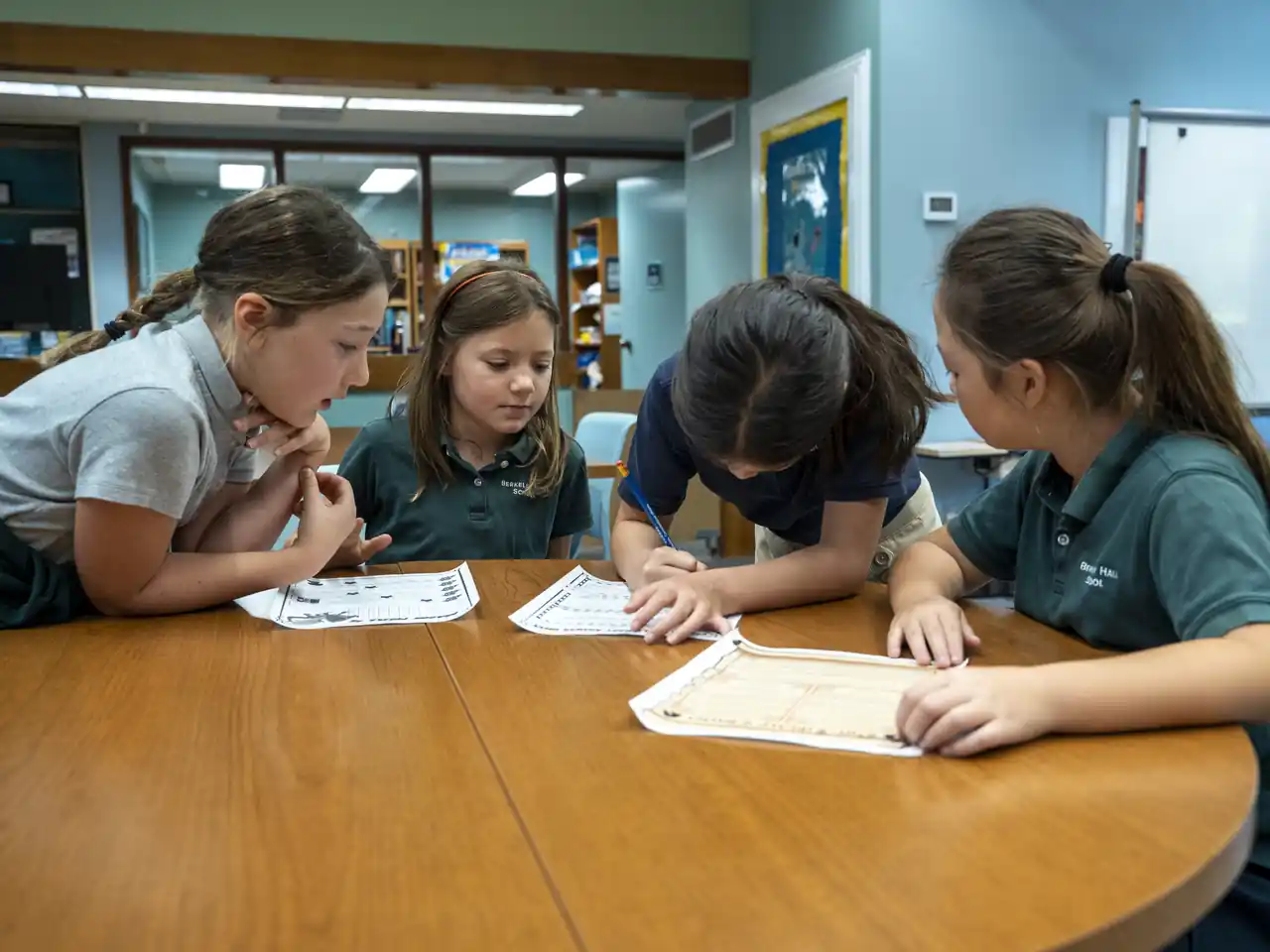 Four students collaborate over activity sheets at a round table.