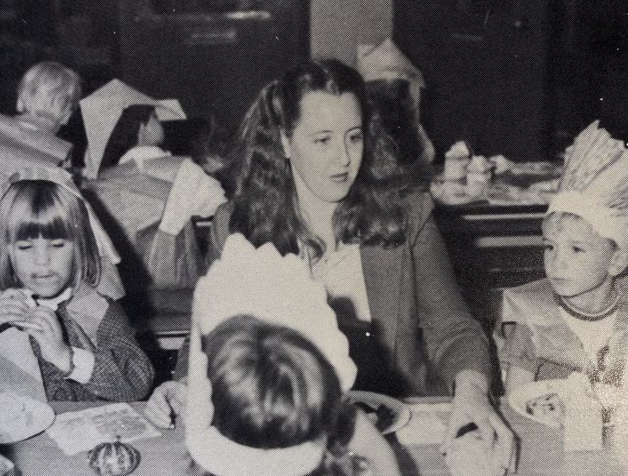 Archival black-and-white photograph of Mrs. DeNisi seated at a classroom table with children wearing paper crowns.