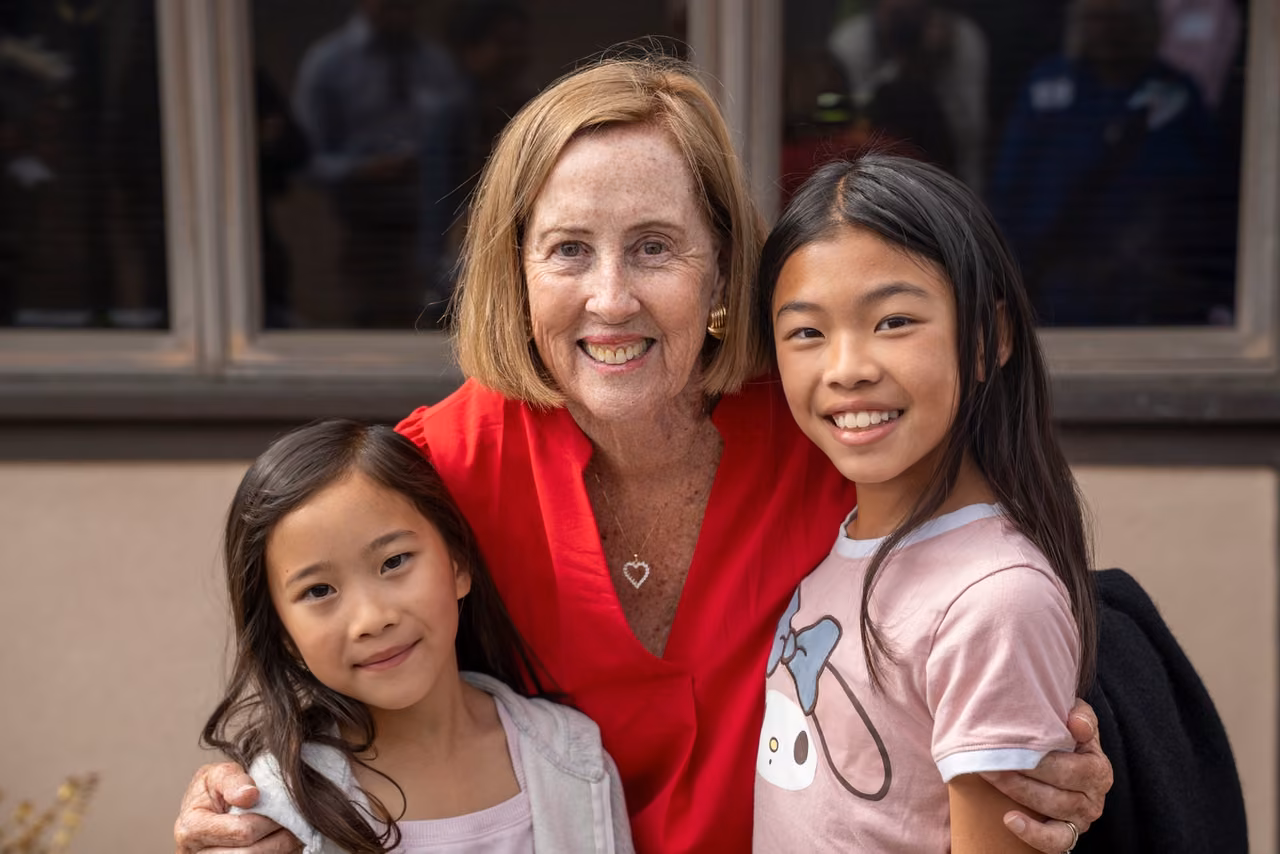 A woman in red smiles alongside two students at the DeNisi Legacy Celebration.