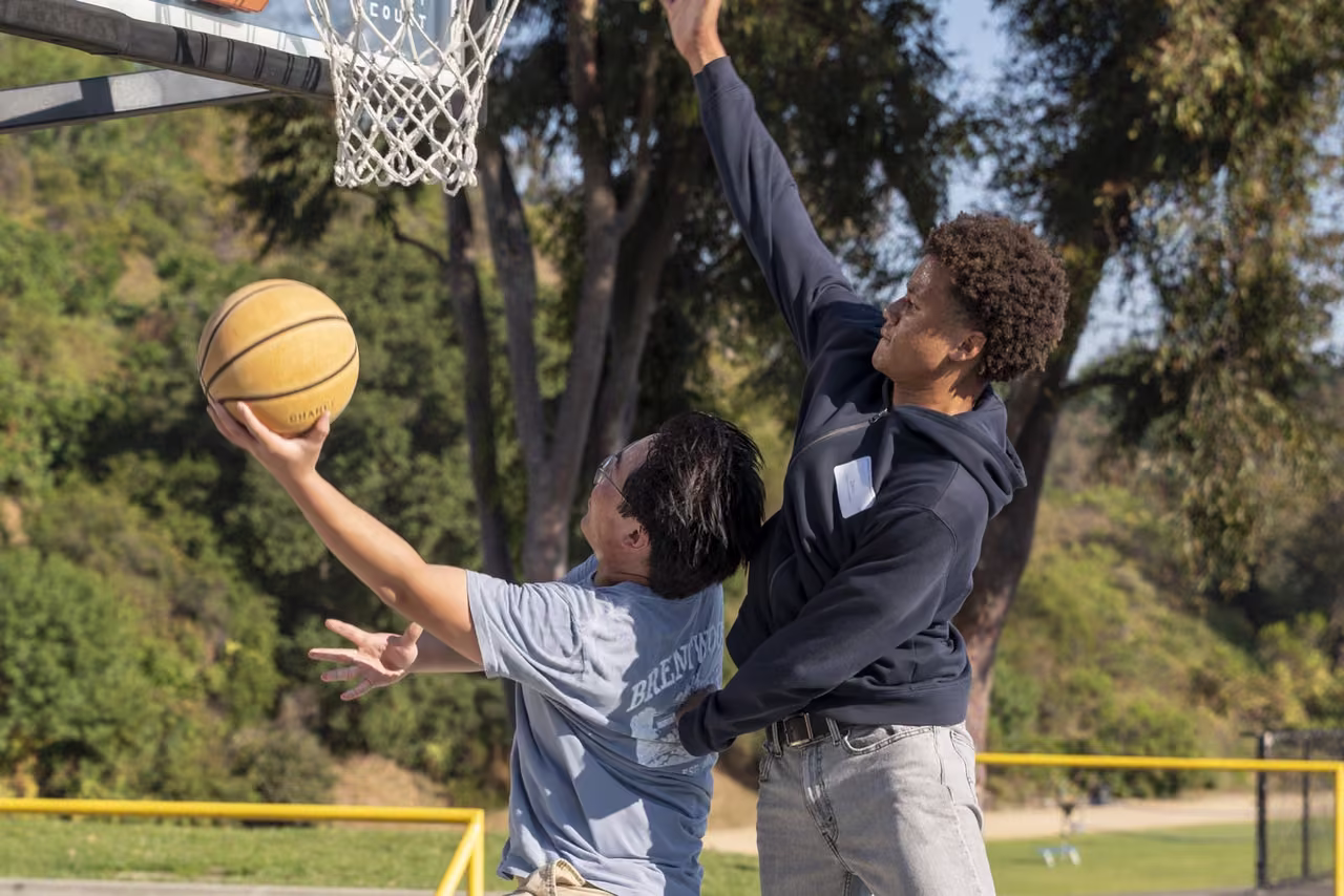One alumnus reaches toward the basket while another jumps to defend.