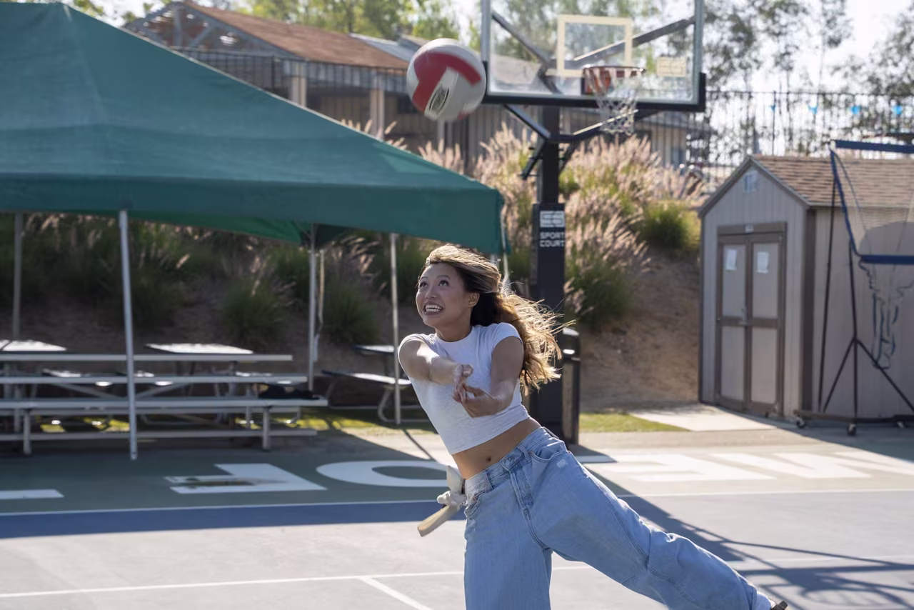 An alumna reaches forward to return a volleyball on the outdoor court.