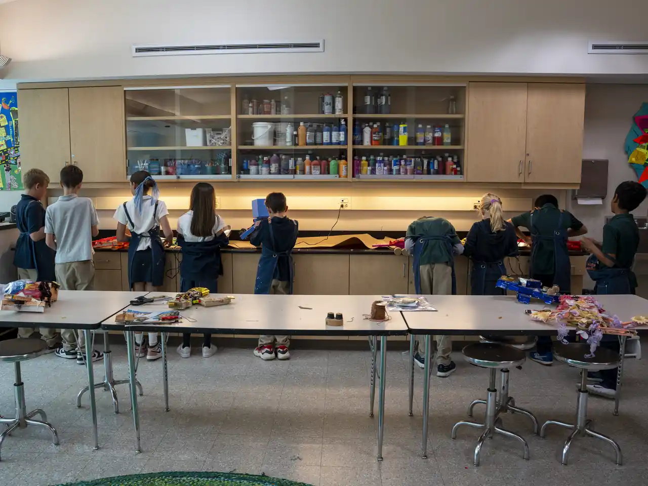 Students work across a bright art studio, seen from behind their project tables.