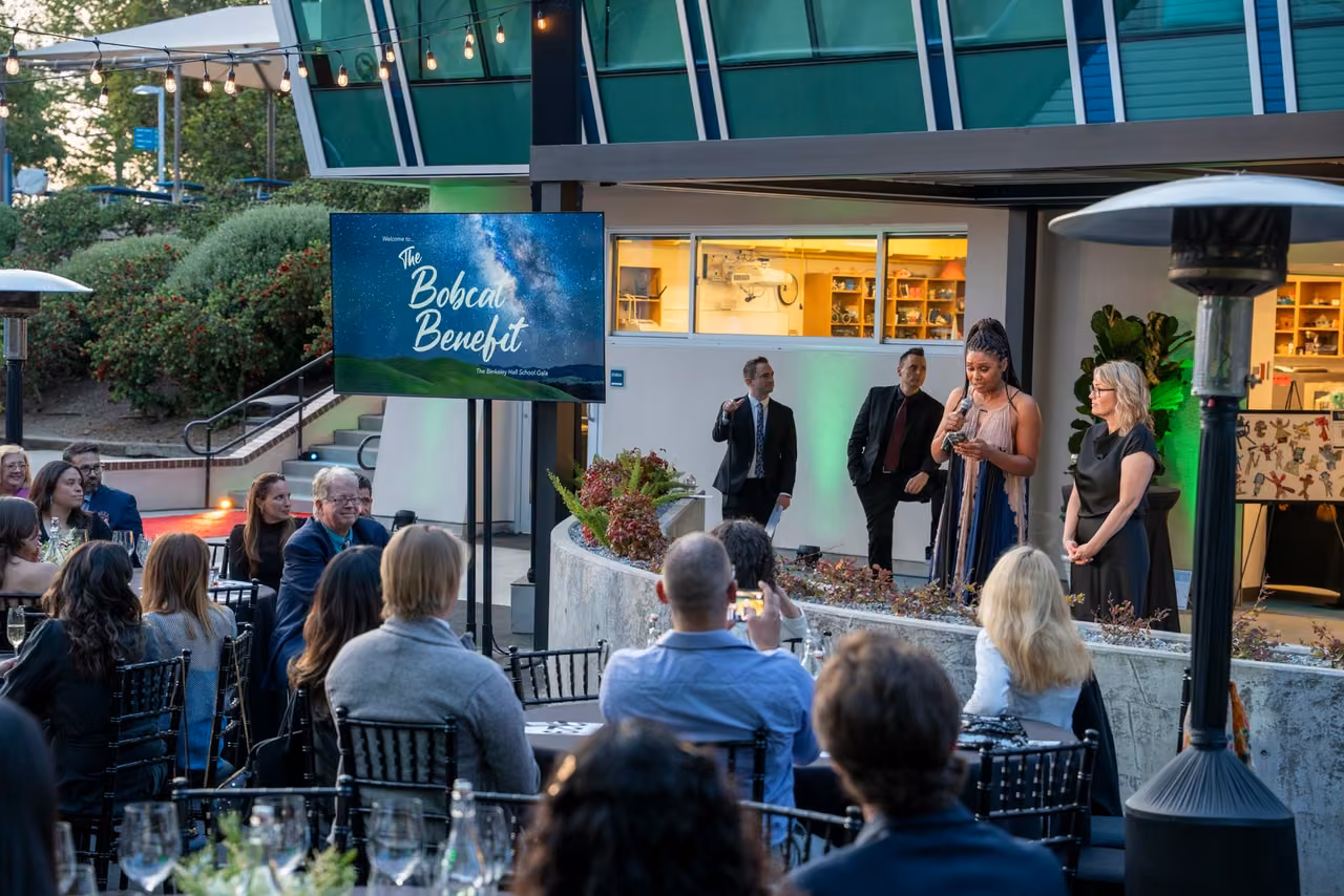 A speaker addresses seated guests beside the Bobcat Benefit display outside the Innovation Lab.