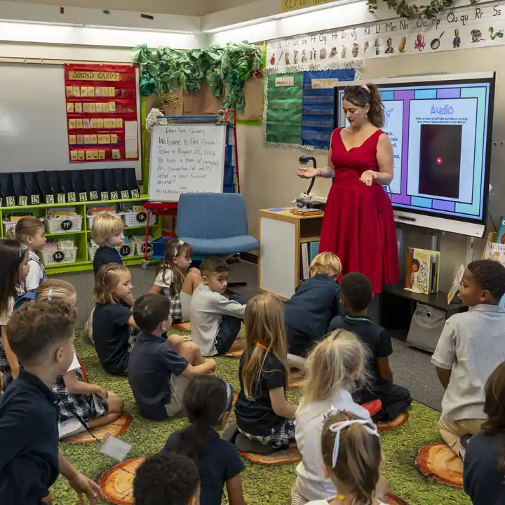 A teacher speaks with a lower-school class gathered on the rug.