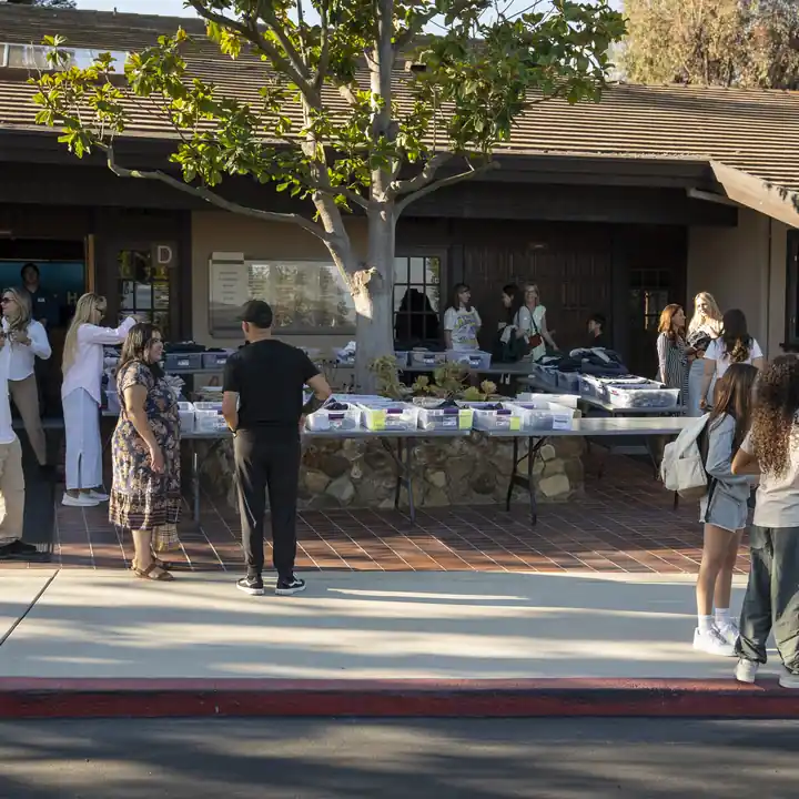 Families browse welcome tables outdoors beneath a campus tree.