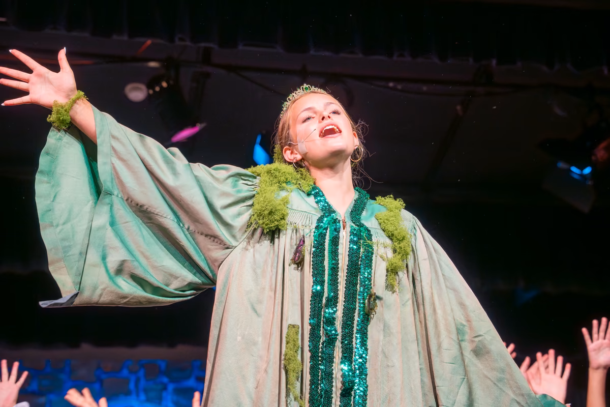 A student in a green costume sings with an outstretched arm during Once Upon a Mattress.